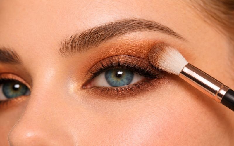 Blending burnt bronze eyeshadow on blue eyes above crease