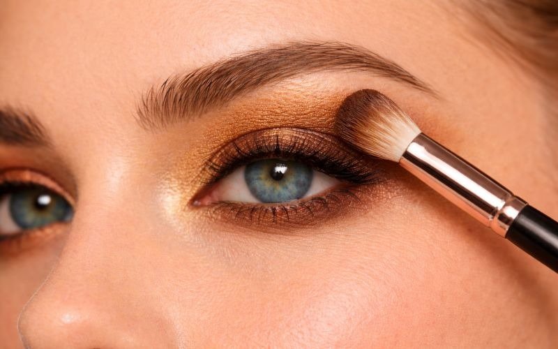 Applying gold eyeshadow into crease for vibrant blue eyes