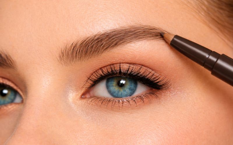 Shaping and filling blue-eyed model’s eyebrows with a brow pencil
